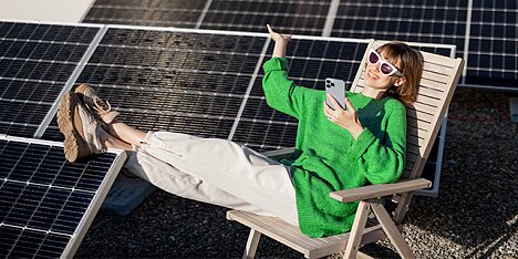 Zrelaksowana kobieta w okularach siedzi na krześle korzystając ze smartfona