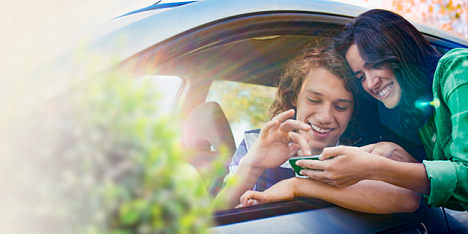 Mężczyzna w aucie i kobieta stojąca obok z zainteresowaniem spoglądają na ekran telefonu korzystając z aplikacji Autostrady