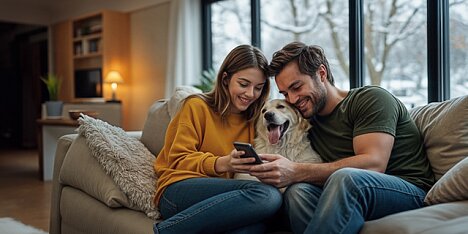 Para w średnim wieku i ich złoty retriever na kanapie przeglądają smartfon szukając informacji o kredycie hipotecznym