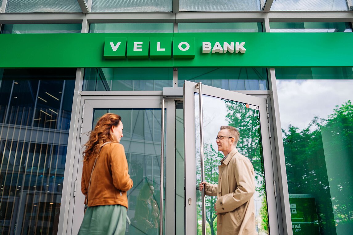Pan otwiera drzwi do placówki VeloBanku i wpuszcza kobietę.