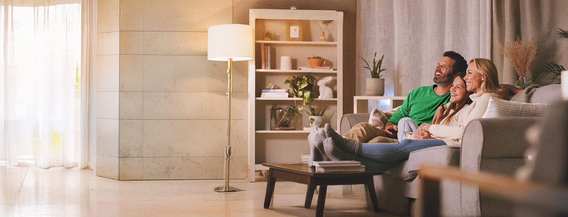 Szczęśliwa trzyosobowa rodzina ogląda telewizję siedząc na kanapie w swoim salonie