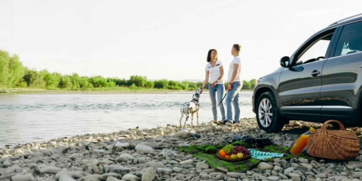 Para spaceruje z psem brzegiem rzeki, w tle widać ich nowe auto