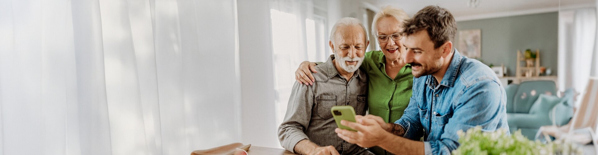 Mężczyzna przedstawia parze seniorów aplikację mobilną na smartfonie nawiązując do braku ograniczeń w dostępności.