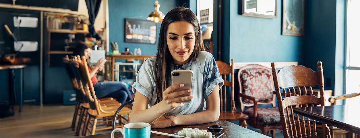 Kobieta w kawiarni przegląda smartfon przy stole z sushi i kawą