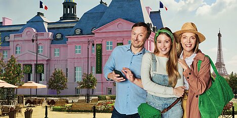 Trzy osoby pozują do zdjęcia przed różowym budynkiem w Paryżu, ciesząc się wakacjami.