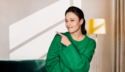 Zadowolona kobieta w zielonym swetrze wskazuje na ofertę kredytu konsolidacyjnego w VeloBank
