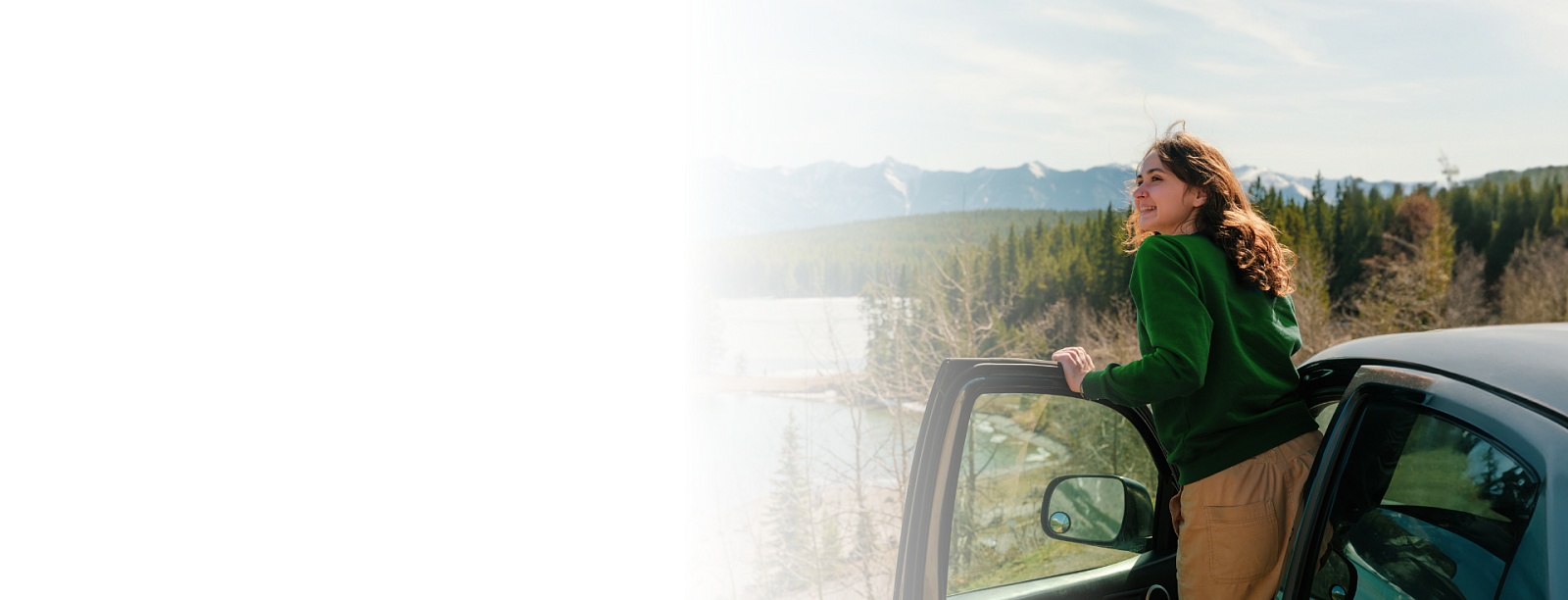 Kobieta obserwuje widok stojąc przy aucie, w tle majestatyczne góry.