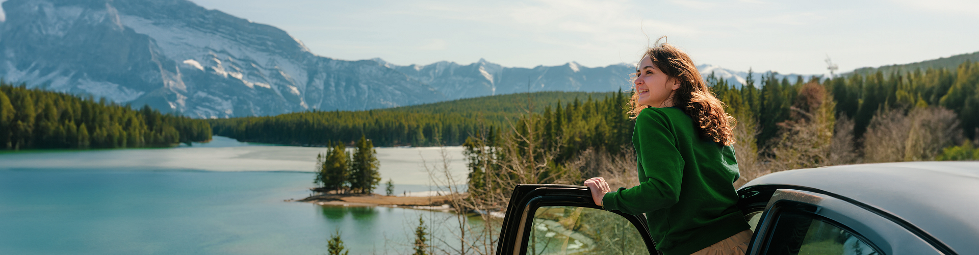 Kobieta obserwuje widok stojąc przy aucie, w tle majestatyczne góry.