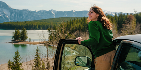 Kobieta obserwuje widok stojąc przy aucie, w tle majestatyczne góry.