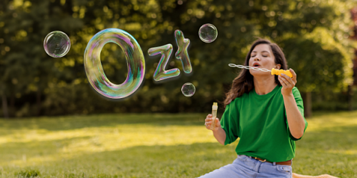 Młoda kobieta w zielonym swetrze wypuszcza bańki układające się w kształt 0 zł