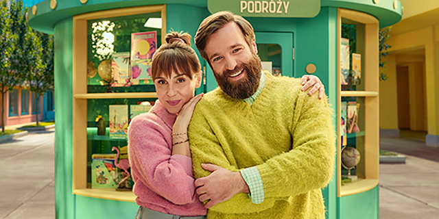 Kolorowo ubrana para uśmiecha się na ulicy otoczona symbolami przedstawiającymi zalety pożyczki gotówkowej w VeloBank